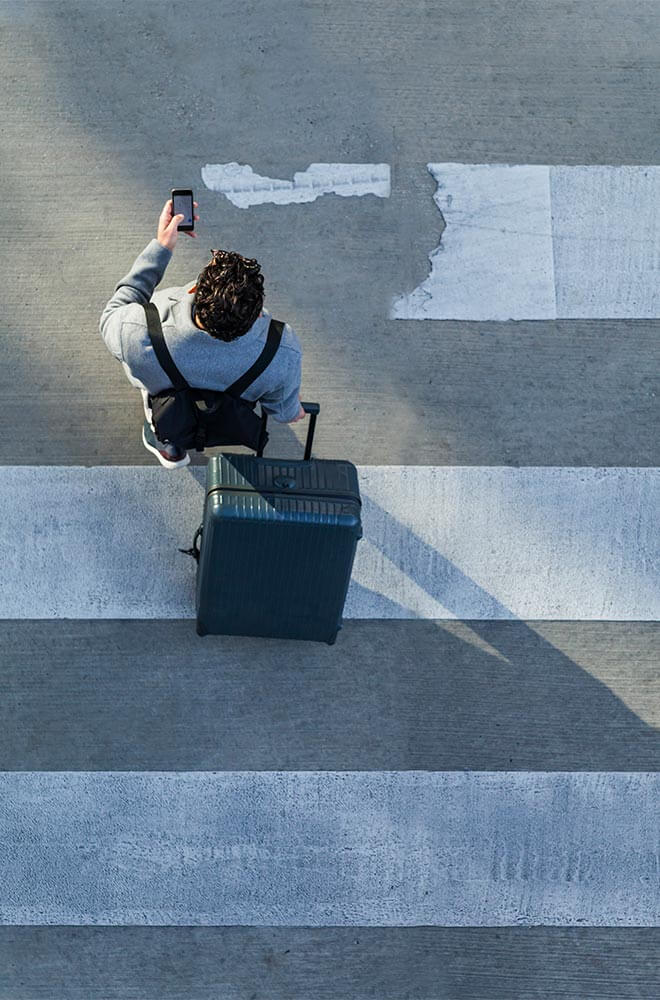 person crossing the sidewalk with a suitcase in one hand, cell phone in the other