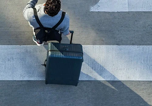 person crossing the sidewalk with a suitcase in one hand, cell phone in the other