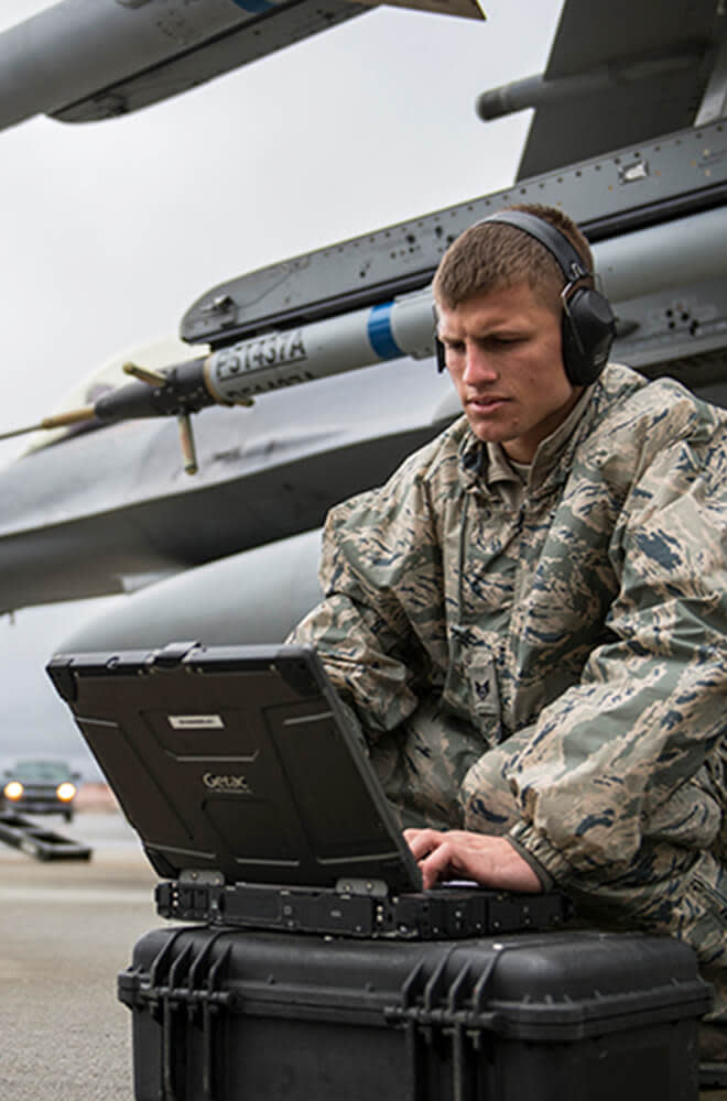 young man in military uniform on laptop in front of a plane