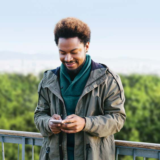 A man looking at his cell phone while standing on a bridge