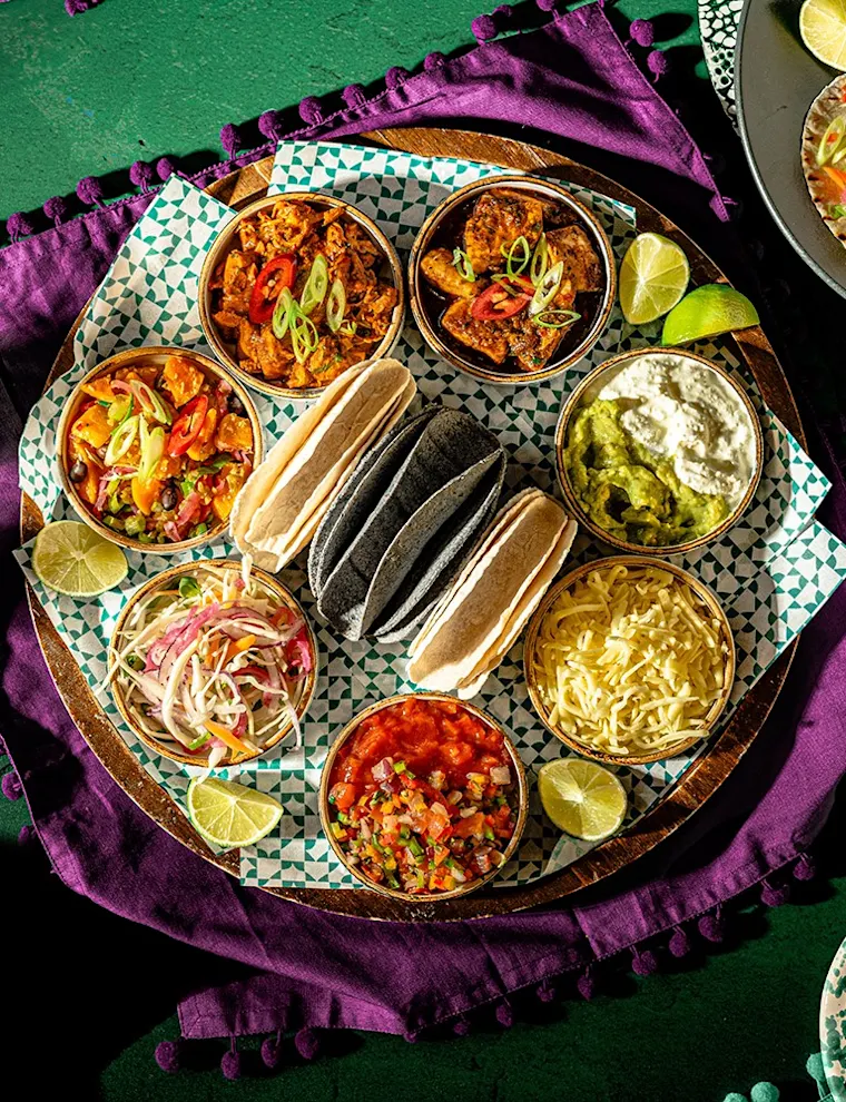 Overhead shot of a table spread with Latin food and cocktails on a blue velvet background
