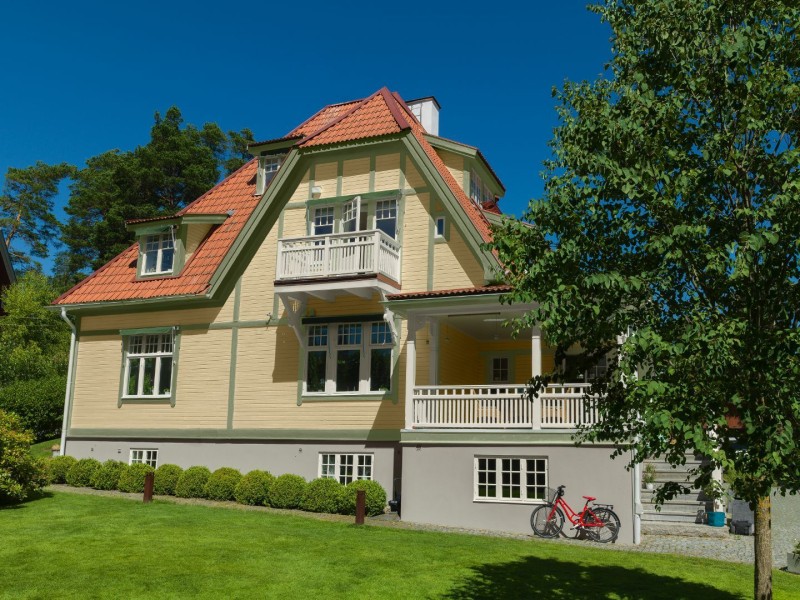 Gult tvåvåningshus med rött tegeltak, vit balkong, grön gräsmatta och röd cykel.