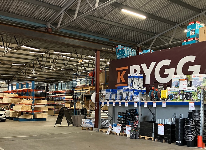 Interiör av hårdvarubutik med staplade träplankor, blåvita verktygslådor och rödbrun BYGG-skylt