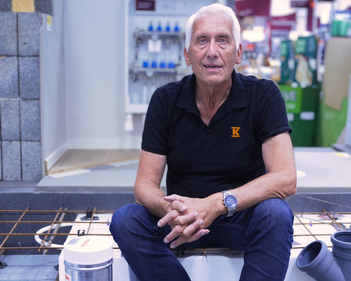 Man i svart piké och jeans sitter på isoleringsblock med armeringsjärn och grå rör i butik