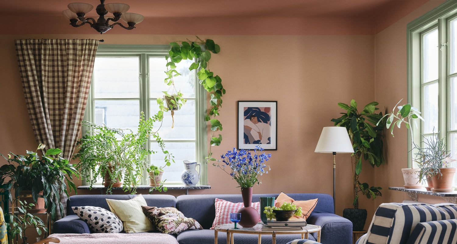 Ljust vardagsrum med aprikosfärgade väggar, gröna växter, blå soffa och blommor på bordet