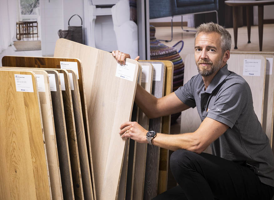 Man i grå pikétröja väljer ljusa och mörka trägolvsprover i butiksmiljö.