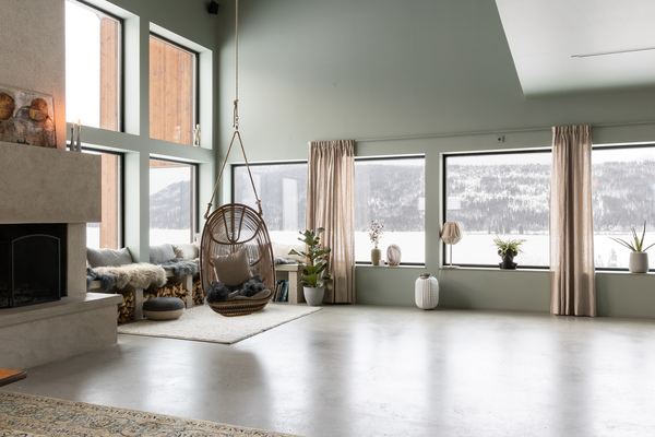 Ljust vardagsrum med mintgröna väggar, stora fönster mot snötäckt vy och hängande rottingfåtölj.