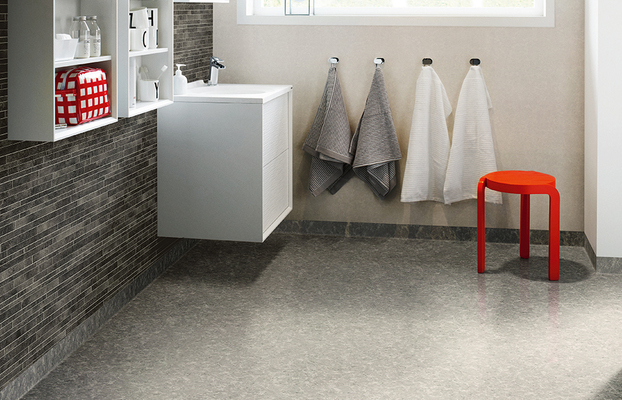 Modernt badrum med vit vägghängd kommod, grå mosaikvägg, fyra handdukar och röd pall.