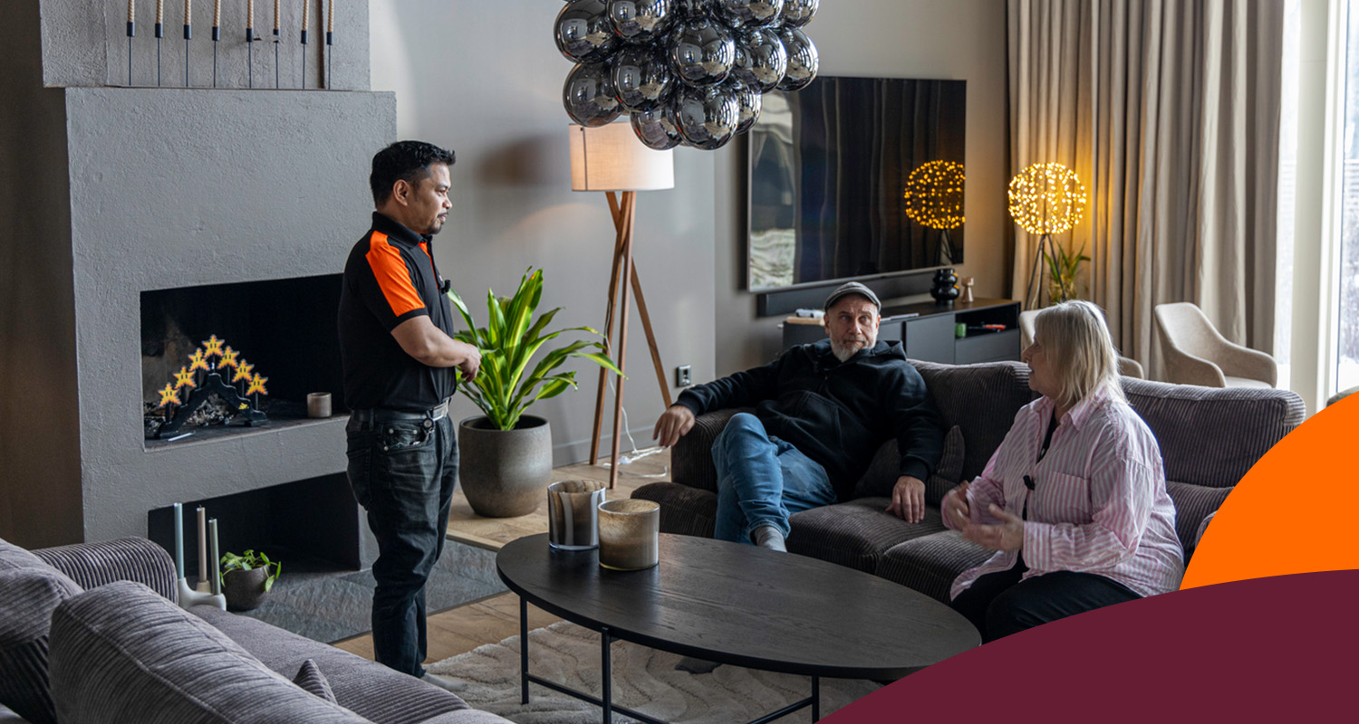 Tekniker i svart-orange vid par i grå soffa i modernt vardagsrum med silverlampa och svart bord