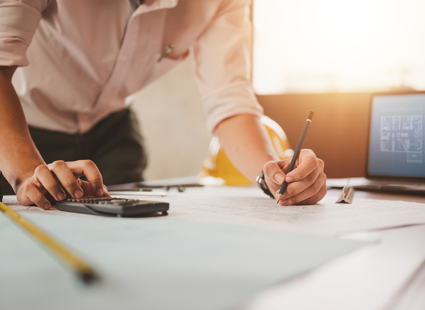 En tekniker arbetar med ritningar och kalkyler för ett solenergiprojekt, omgiven av mätverktyg och digitala hjälpmedel.