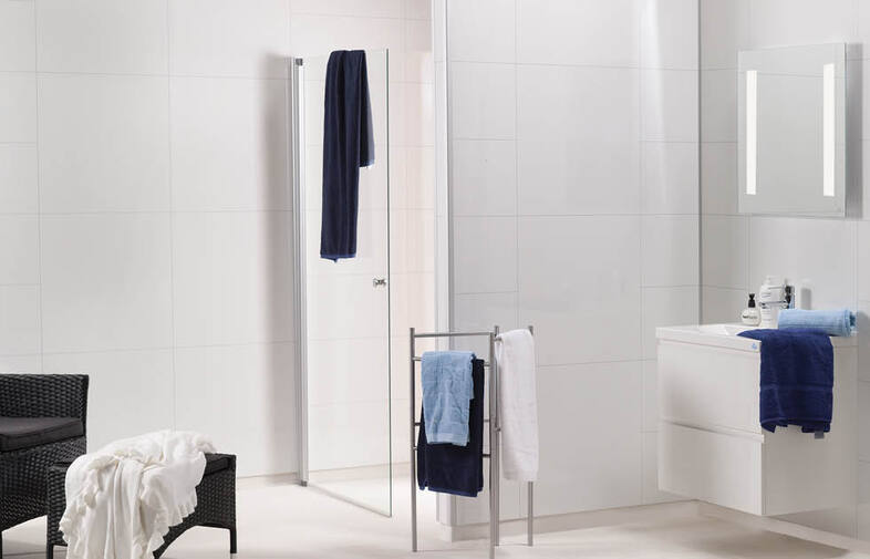 Vitt kaklat badrum med glasdusch, handdukstativ med blå/vita handdukar, vit kommod med spegel.