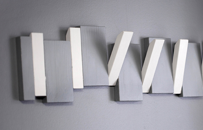 Vägginstallation med omväxlande grå och vita rektangulära träblock på grå bakgrund.