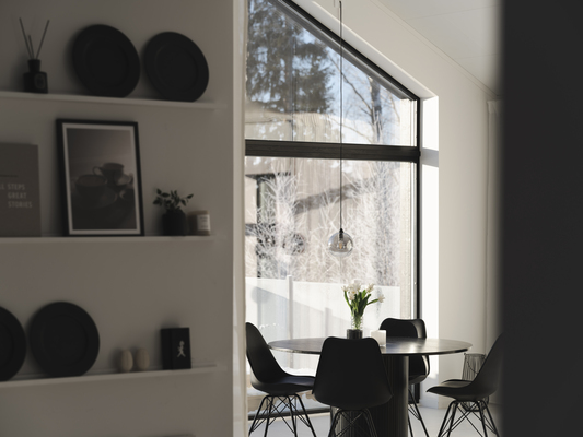 Ljus matsal med svart runt bord, stolar, hylla med svarta tallrikar, vas med tulpaner, fönster mot snöig skog