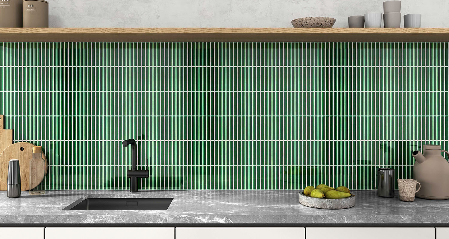 Modern köksbänk med grön mosaik, svart kran, marmorbänk, skärbrädor och fat med päron.