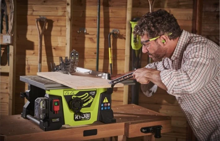 Person sågar en träskiva på grön Ryobi bordscirkelsåg i träverkstad.