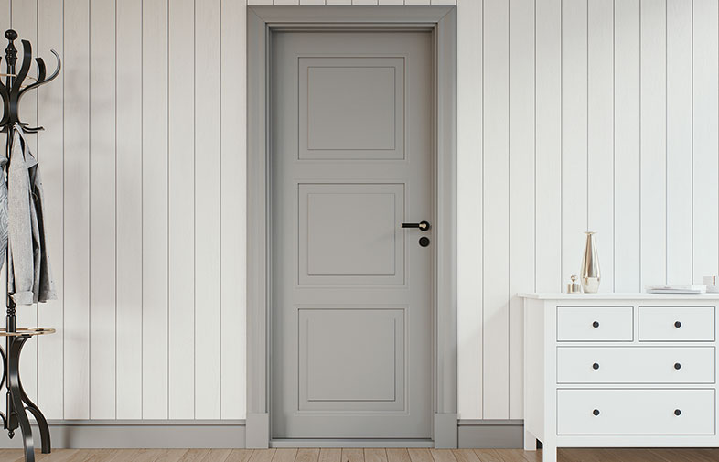 Minimalistisk hall med grå dörr i vit träpanel, svart klädförvaring till vänster, vit byrå höger.