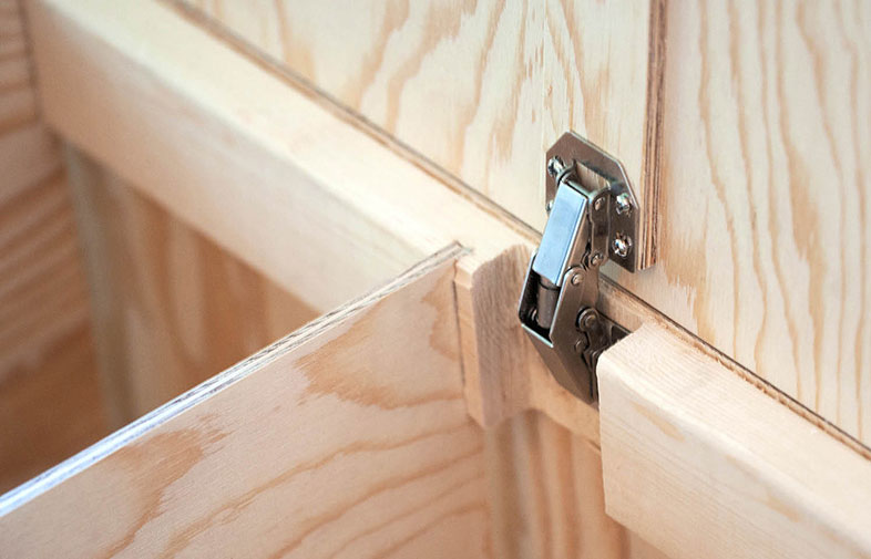 Närbild av ljus träskåpsdörr och silverfärgat metallgångjärn.