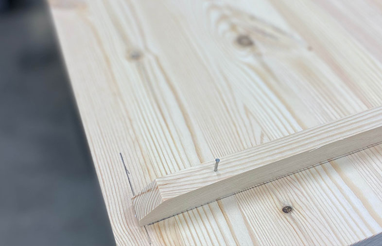 Ljust furubord med snedskuren list och en uppstickande skruv inuti.