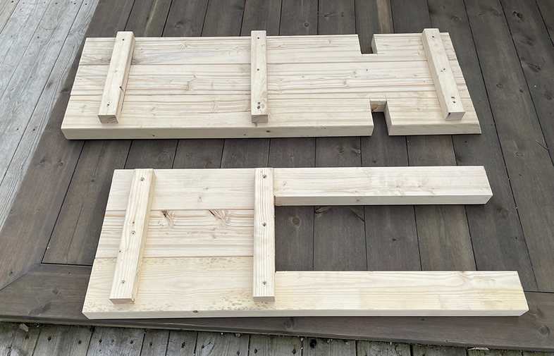 Två ljusa, obehandlade träplankor med tvärslåar på mörkbrunt utomhusdäck.