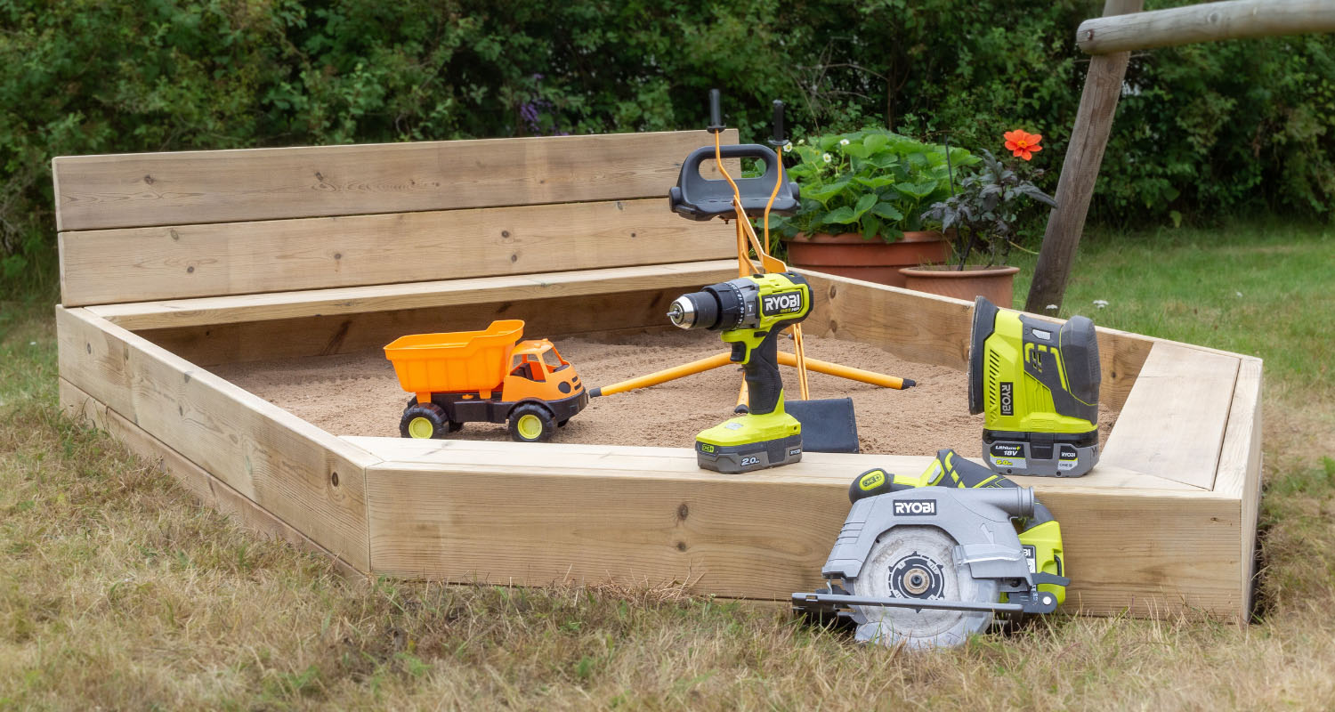 Trä-sandlåda med orange leksakslastbil, gröna Ryobi-elverktyg och blomkruka.