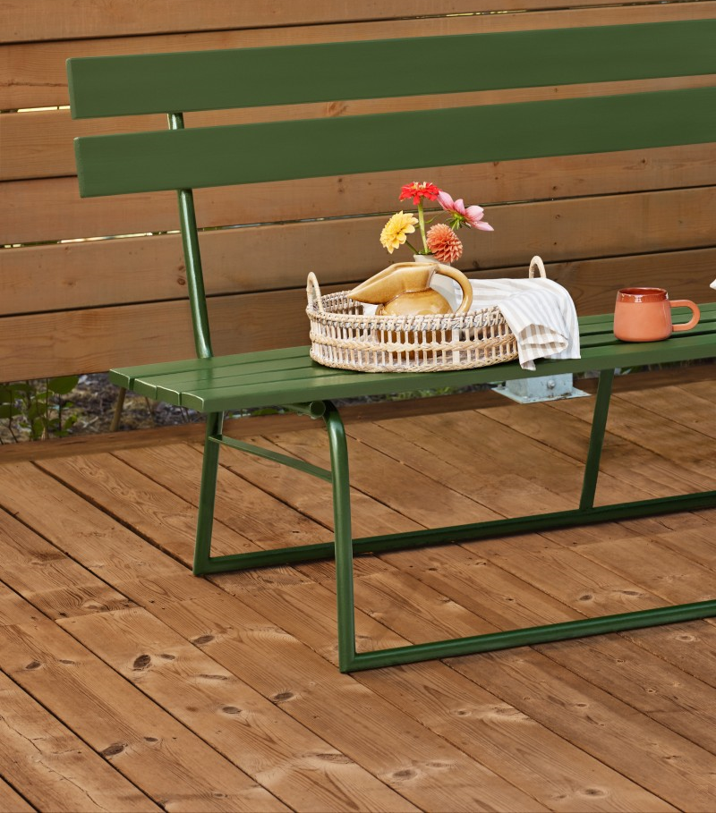 Grön bänk på trädäck med rottingbricka, kanna, randig duk, färgglada blommor och kopp