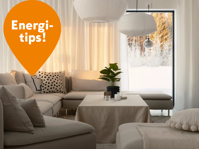 Ljust vardagsrum med grå soffa, bordsväxt, snölandskap utanför och orange bubbla ’Energi-tips!’
