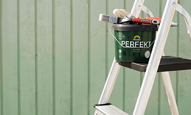 Vit stege med grön "Perfekt"-färgburk och penslar framför ljusgrön panelvägg.