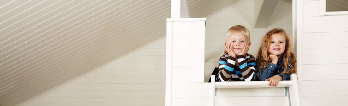 Två barn lutade mot ett vitt räcke i ett ljust rum med vit träpanel och snedtak.