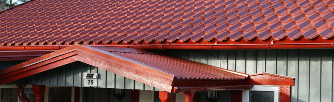 Rött plåttak och veranda mot grå träfasad, husnummer 29 synligt under taket