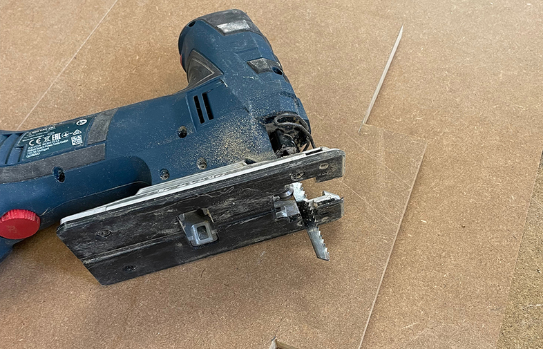 Mörkblå sticksåg med röd ratt och synligt blad liggande på träskiva med sågspån.