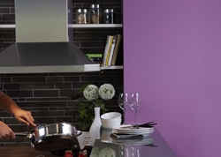 Person steker mat i modernt kök med mörkt kakel, glas, tallrikar och lila vägg.