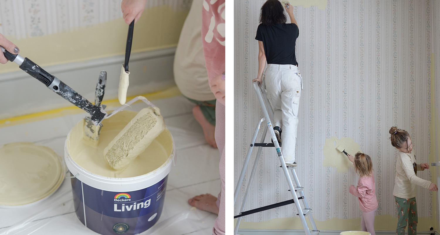 Mor på stege och två barn målar blommig tapet med ljusgul färg, färghink i förgrunden.