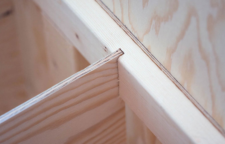 Närbild av hyllplan i ljusbeige trä inskjutet i spår i plywoodpanel