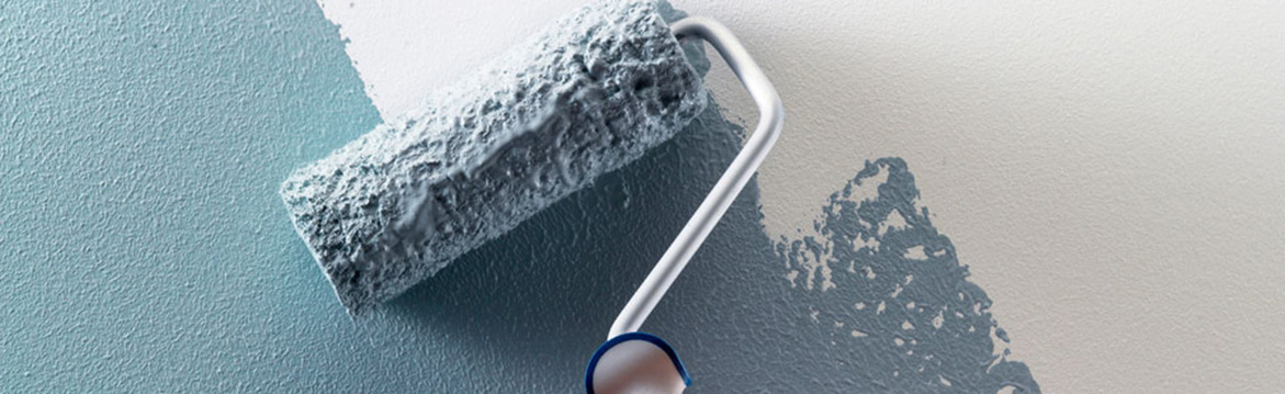 Färgroller täckt av ljusblågrå färg målar vägg från vitt till blågrönt.