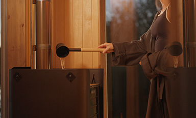 Person öser vatten med träskopa på het stenkamin i varm träbastu.