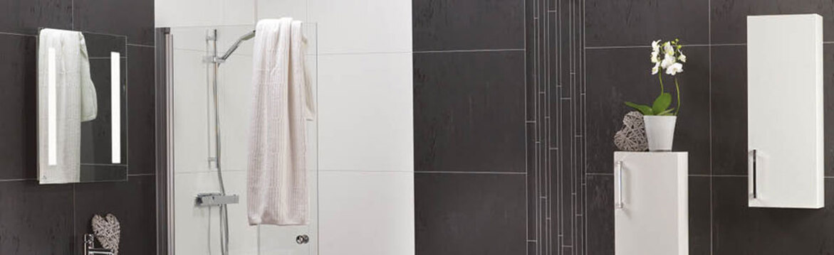 Modern badrum med svart kakelvägg, glasdusch med vitt badlakan, vita skåp och orkidé.