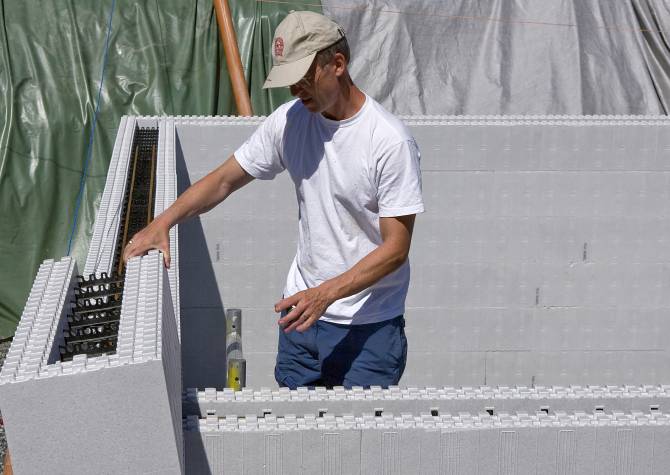 Arbetsman monterar vit cellplastvägg på byggarbetsplats med grön presenning.