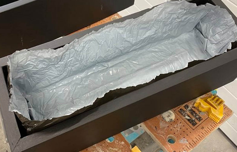 Svart rektangulär trälåda med grå plastfoder på snickarbänk.