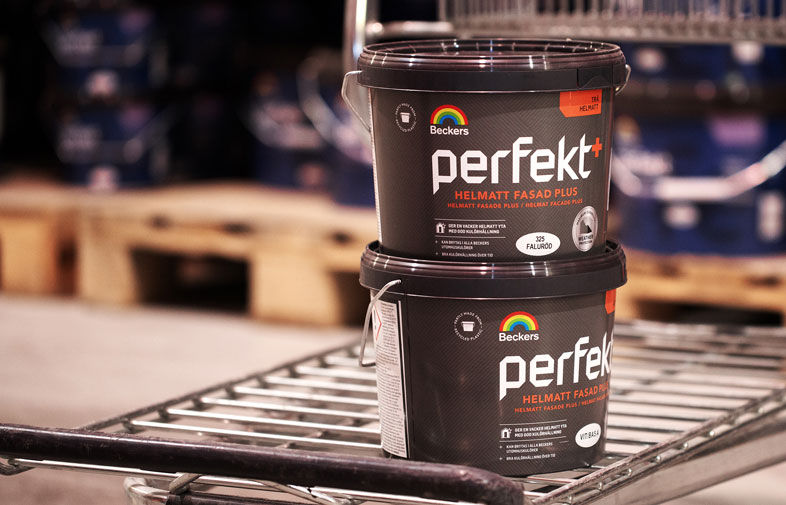 Två svarta Beckers Perfekt+ färghinkar med regnbågslogga staplade på metallhylla i lager.