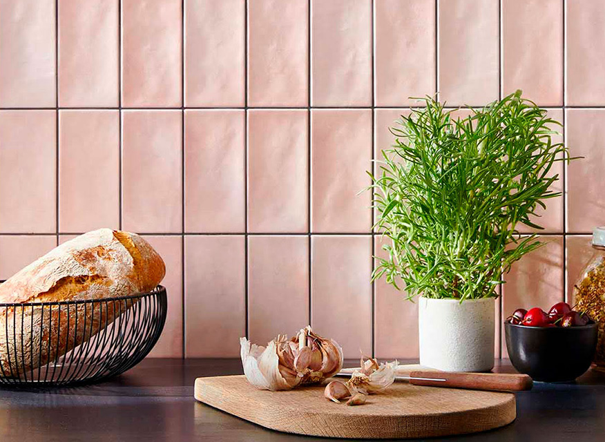 Köksbänk i trä med rosa kakel, brödkorg, vitlök på skärbräda och liten kryddväxt.