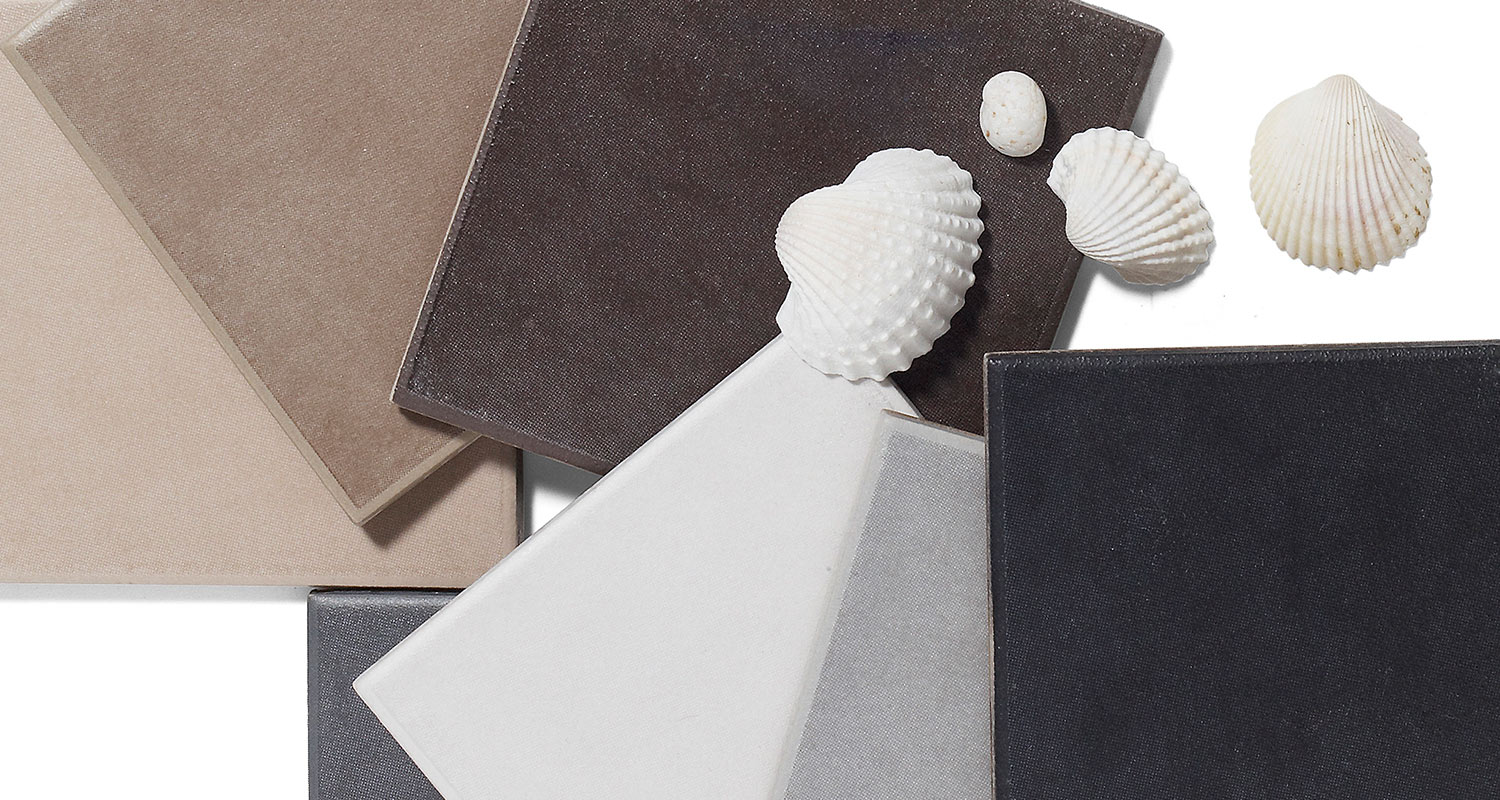 Överlappande kakelplattor i beige, brun, grå och svart med vita snäckskal på vit bakgrund.