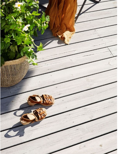 Ljusgrå trädäck med bruna sandaler, oranget tyg och korg med vita blommor.