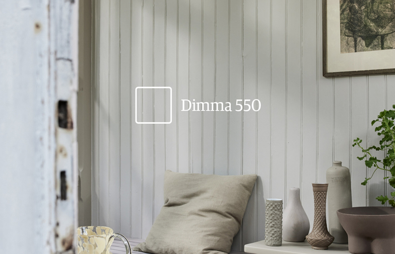 Ljust hörn med vitmålad träpanel, öppen vit dörr, beige kudde, keramikvaser och grön växt.