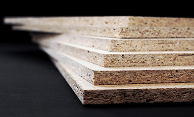 Närbild på en stapel ljusbeiga spånskivor i trappstegsform mot mörk bakgrund