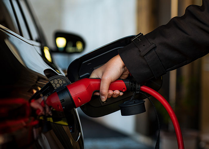 Närbild på hand i svart ärm som kopplar in röd laddkabel i svart elbil.