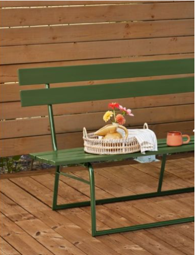 Grön metallbänk på trätrall, rottingkorg med bananer, färgglada blommor och orange kopp