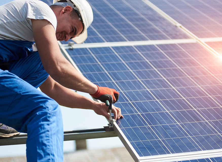 En montör i skyddsutrustning arbetar med att säkra solpaneler under soligt väder.