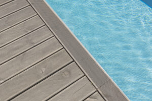 Grå trädäck vid klarblått, glittrande poolvatten.
