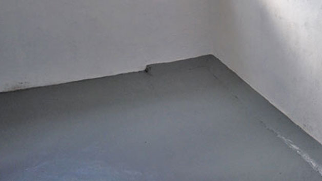 Tomt hörn med slätt gråmålat betonggolv och vit skrovlig vägg.