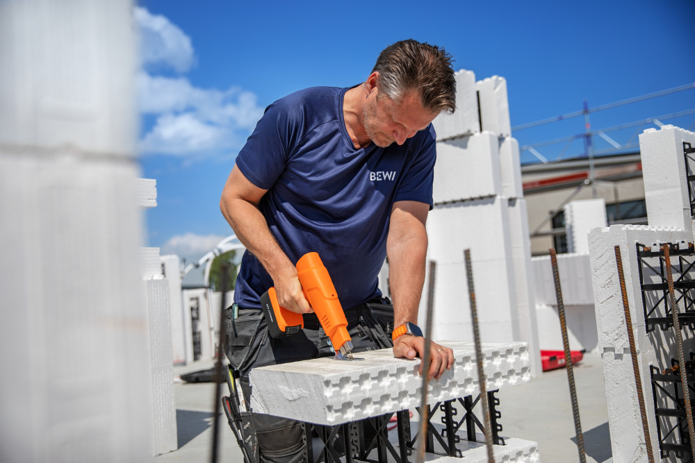 Byggarbetare limmar vita cellplastsblock med orange värmepistol under klarblå himmel